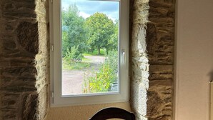 A room with a stone wall and a window with a view of a garden and a path.