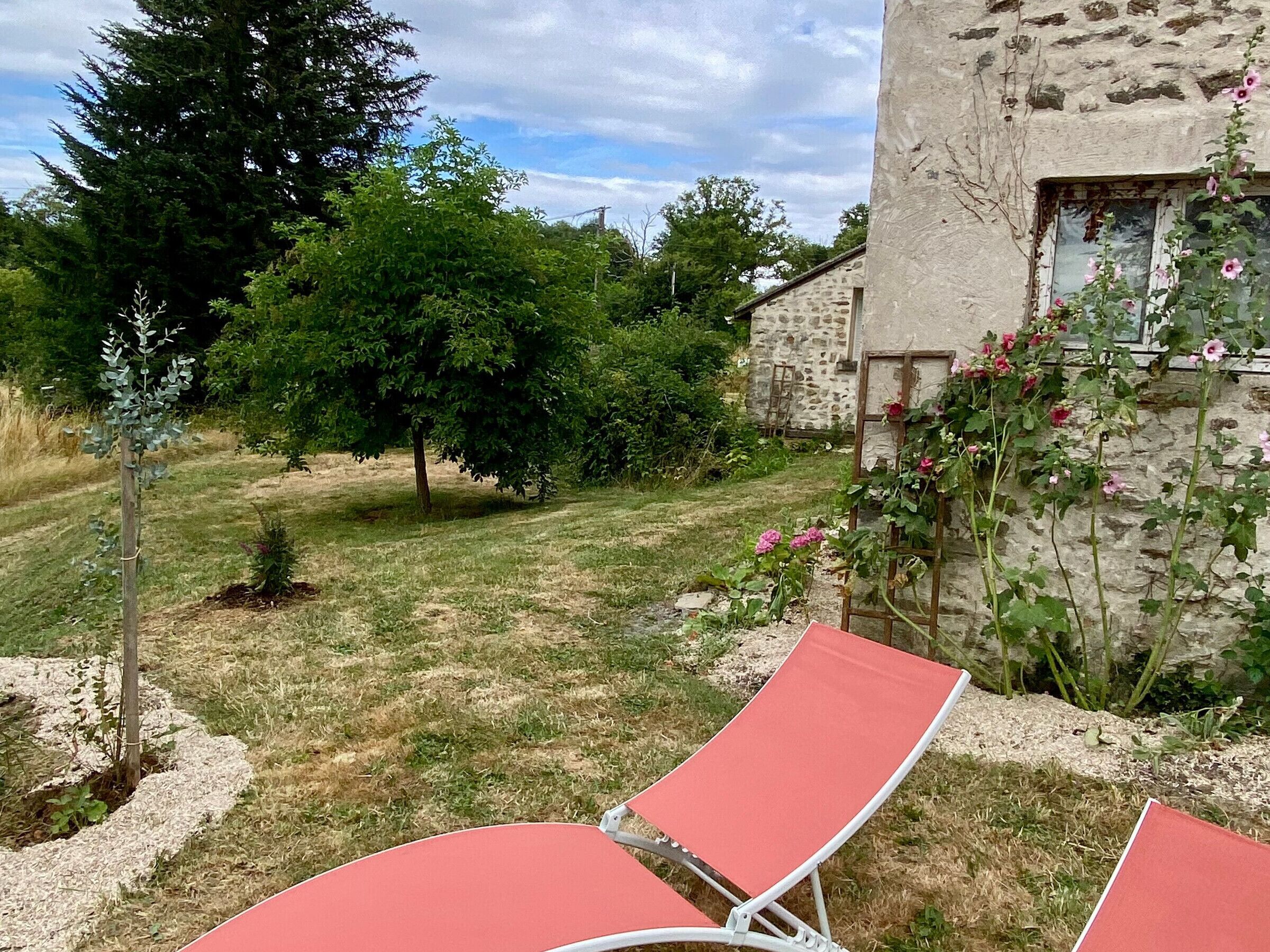 A garden with a stone wall, a red lounge chair, and a tree.