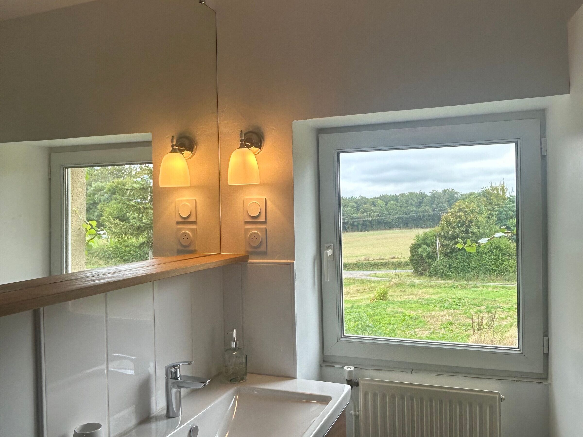 A bathroom with a large window, a mirror, a sink, and two wall-mounted lights.