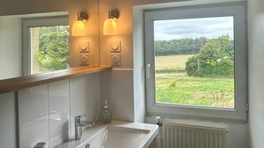 A bathroom with a large window, a mirror, a sink, and two wall-mounted lights.