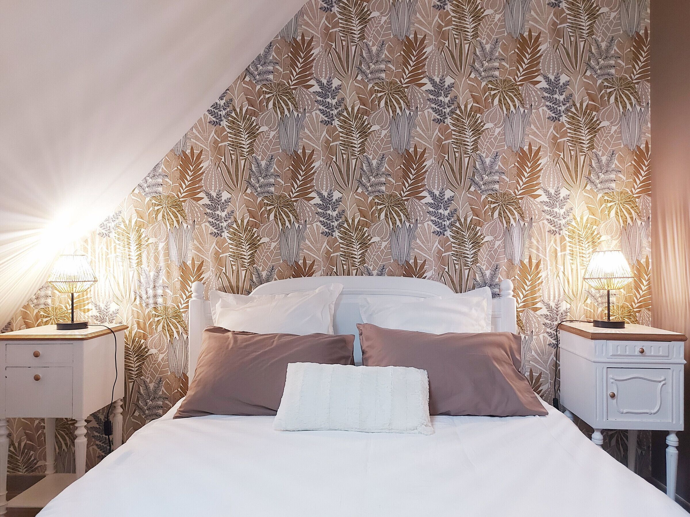 Un dormitorio con una cama grande, dos mesitas de noche con lámparas y un estampado de flores en el papel tapiz.