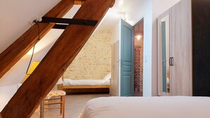 Une chambre avec un plafond en pente, un lit, une chaise et une armoire.