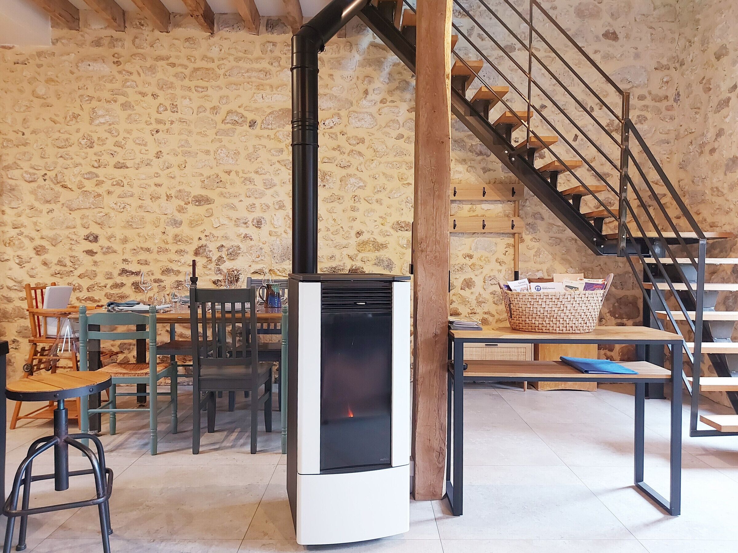 A rustic interior with a stone wall, a modern fireplace, wooden furniture, and a staircase.