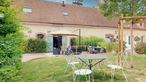 Un espace patio avec une table et des chaises, un coin salon abrité et une vue sur un bâtiment doté d’un toit en tuiles.