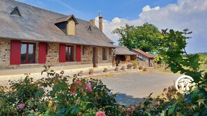 A stone farmhouse with red shutters, a sloped roof, and a garden with potted plants and roses. - Country house with terrace and fireplace, accessible for PRM, near water activities (Saint-Aignan-sur-Roë)