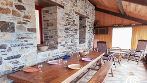 A rustic stone wall with a wooden table set for dining, stone flooring, and wooden chairs. - Country house with terrace and fireplace, accessible for PRM, near water activities (Saint-Aignan-sur-Roë)
