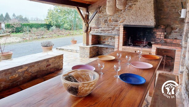 An outdoor dining area with a stone fireplace, wooden beams, and a view of the surrounding landscape. - Country house with terrace and fireplace, accessible for PRM, near water activities (Saint-Aignan-sur-Roë)