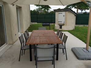 An outdoor patio with a wooden table and chairs, a covered area, and a small shed in the background. - Bright cottage with wifi, pets allowed, parking, near Château-Gontier (Peuton)