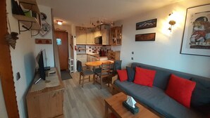 A compact living space with a dining area, kitchenette, and a sofa with red cushions.