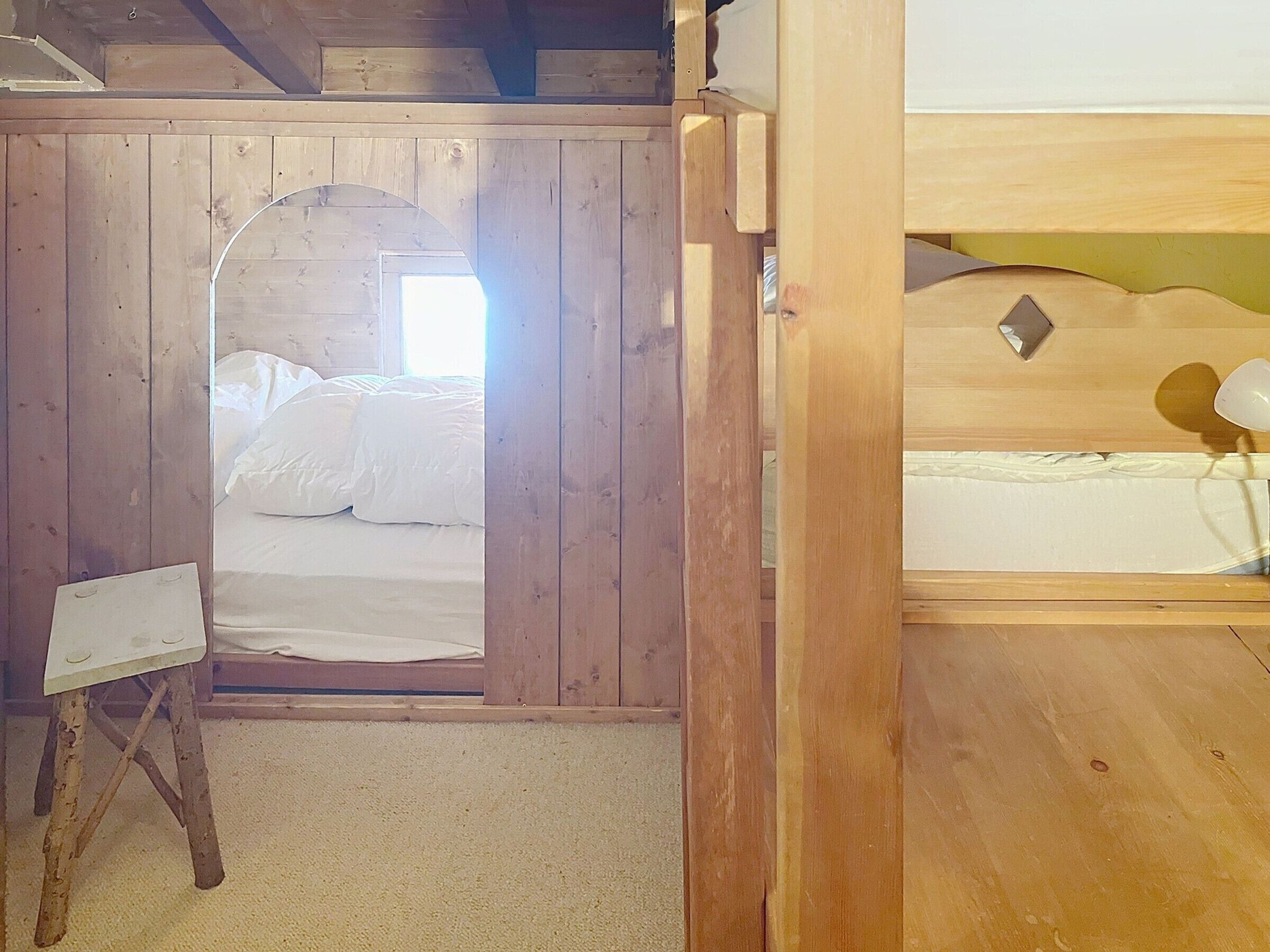Una habitación de madera con una cama, una mesita y un ventanal.