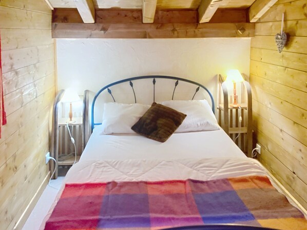 Una habitación de cabaña de madera con cama, mesita de noche y lámpara fijada a la pared.