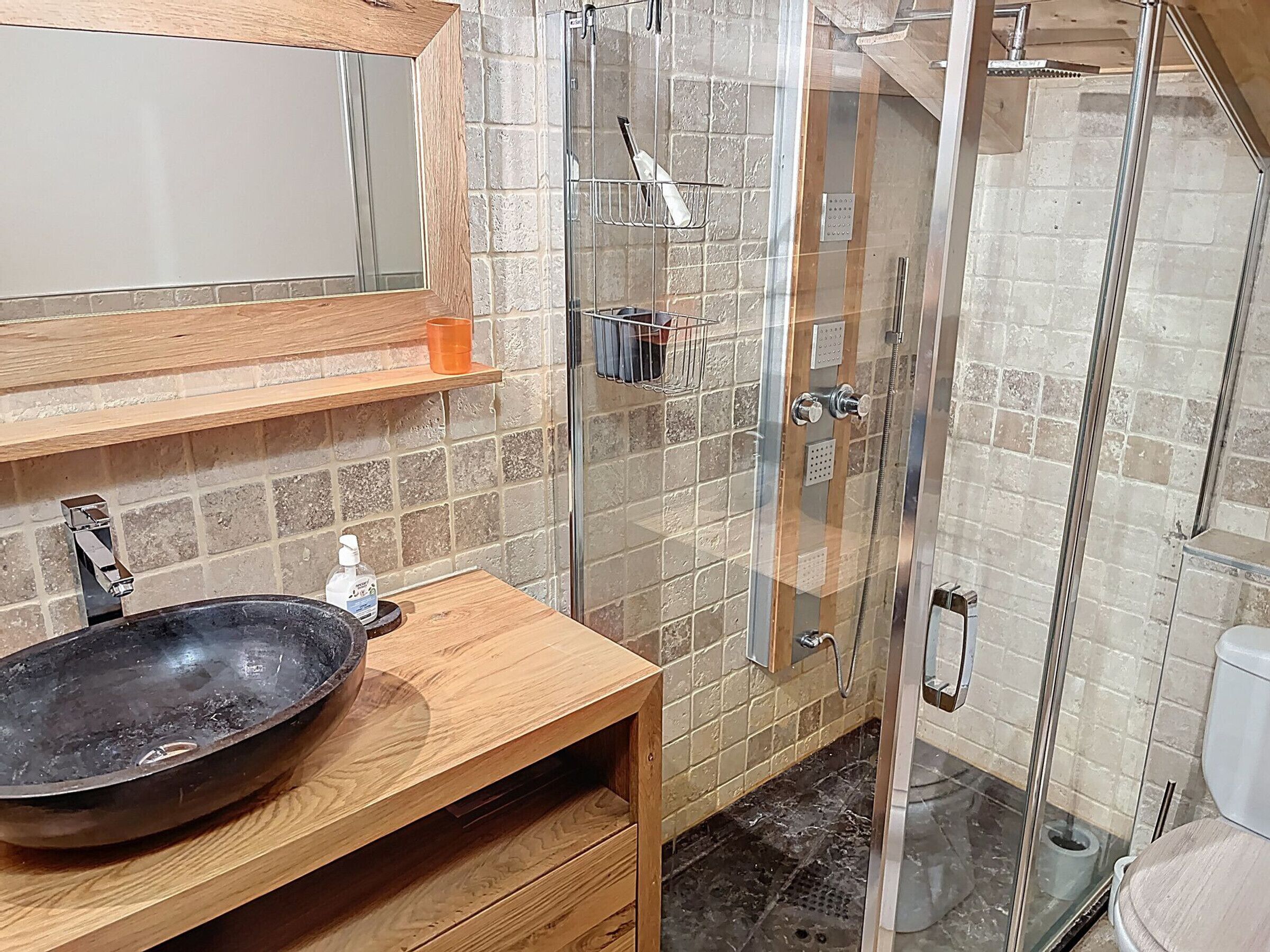 A bathroom with a wooden vanity, a large basin, a glass shower enclosure, and a toilet.