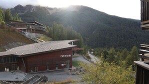 A building named 'Patinoire' with a sloped roof, surrounded by a mountainous landscape and trees. - Cozy studio for 6, in the heart of the resort (Les Orres)