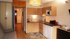 A compact kitchen with wooden cabinets, a microwave, and a sink. There is a small round table and a sofa in the adjacent living area. - Cozy studio for 6, in the heart of the resort (Les Orres)