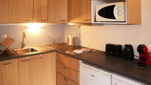 A compact kitchen with wooden cabinets, a built-in microwave, a sink, a toaster, a coffee maker, and a dishwasher. - Cozy studio for 6, in the heart of the resort (Les Orres)