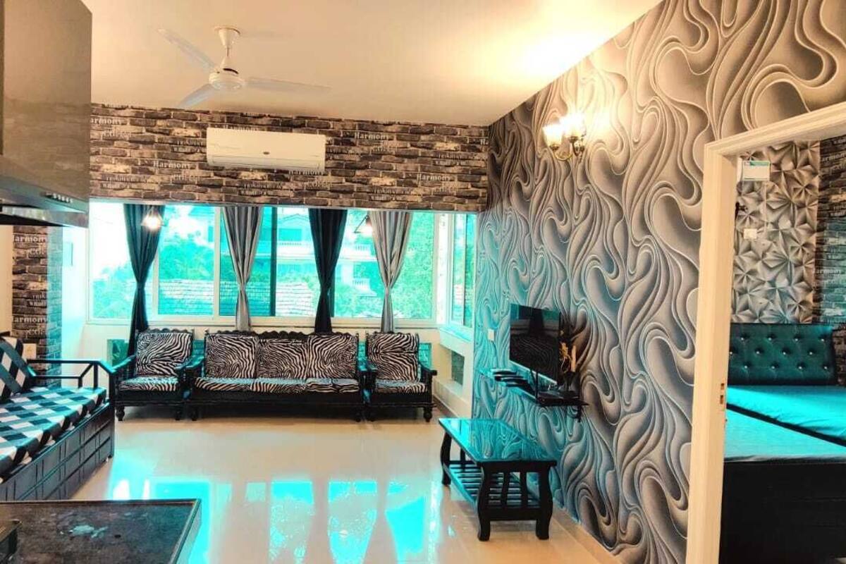 A spacious living room with a sofa set, a coffee table, and a TV. There is a ceiling fan and a window with curtains.