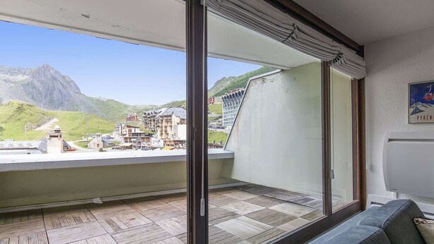 Ein Balkon mit Blick auf eine gebirgige Landschaft, einem Holzboden und einem grauen Sofa.