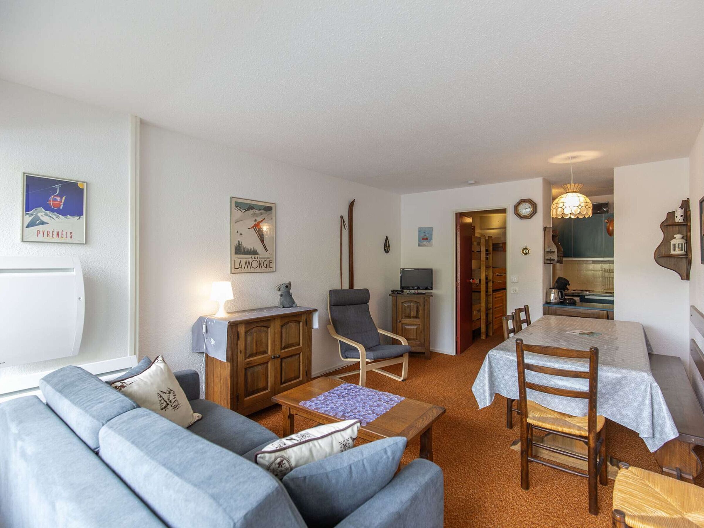 Una sala de estar acogedora con sofá, sillón y mesa de comedor. Se ve una cocina a través de un umbral abierto.