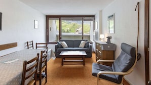Ein gemütliches Wohnzimmer mit einer Couch, einem Esstisch und Stühlen. Ein großes Fenster bietet Blick ins Freie.