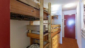 Ein kleines Zimmer mit einem Etagenbett, einem Schreibtisch und einer Tür zu einem weiteren Raum.