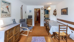 Ein gemütliches Zimmer mit einem Holztisch, einem blauen Stuhl, einem Holzschrank und einem Skidekor-Poster an der Wand.