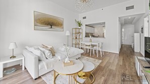 Een moderne woonkamer met een witte bank, gouden accenten, een kroonluchter en een eethoek met witte meubels.