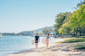 A beach with a couple walking, a boat, and a building in the background.