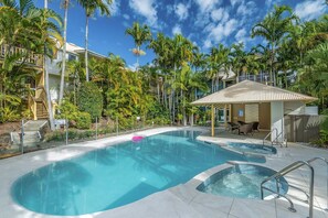 A swimming pool with a hot tub, surrounded by palm trees and a covered seating area.