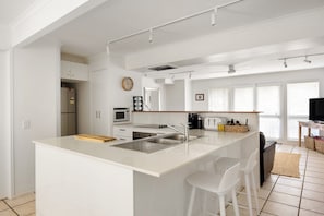 Una cocina moderna con una isla central, armarios blancos, microondas, cafetera y tostadora.