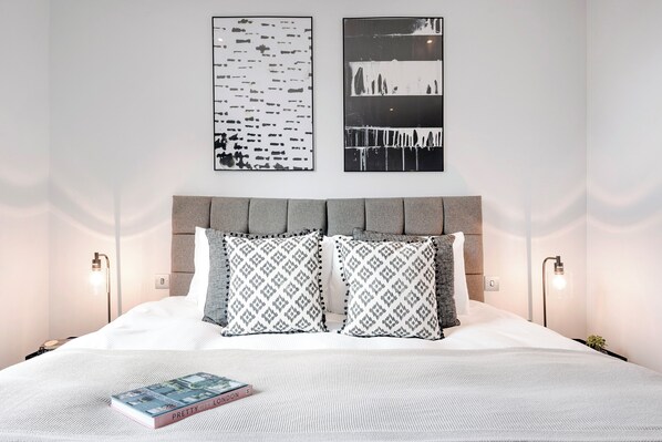 A modern bedroom with a large bed, two side tables, and wall-mounted lamps.