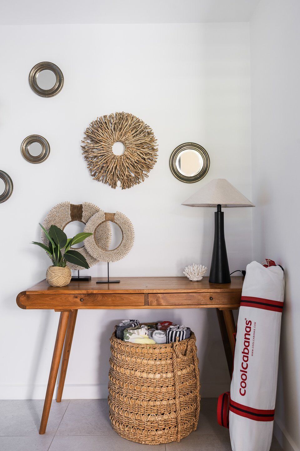 A wooden desk with a lamp, decorative wall mirrors, and a woven basket.