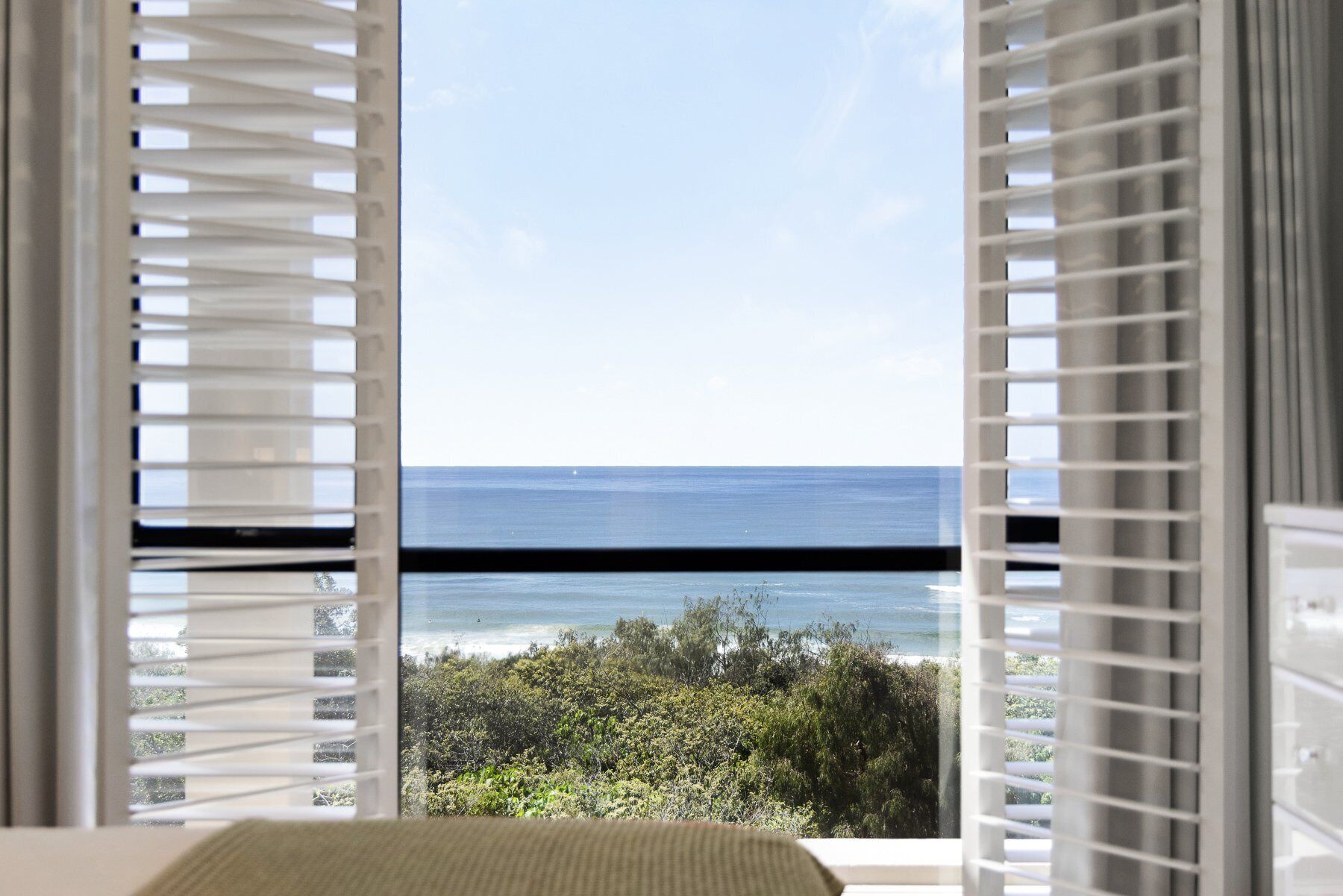 A room with a view of the ocean through open window blinds.