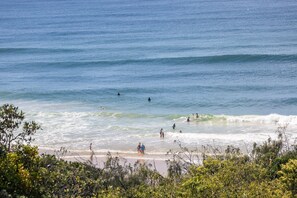 A beach with people swimming and walking along the shore. - Postcard on Sunrise Ocean Views walk to Beach (Noosa)