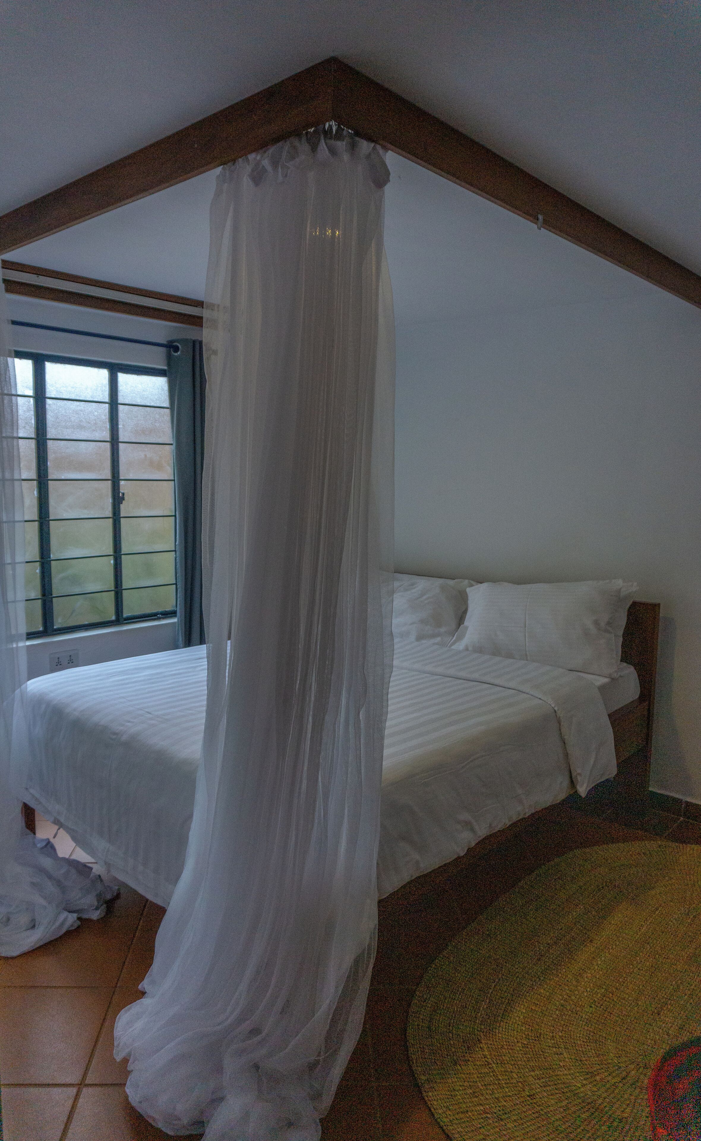 A bedroom with a bed, a window with curtains, and a wooden ceiling.