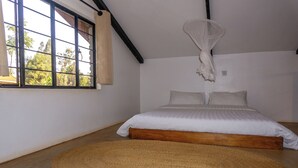 A bedroom with a large bed, a woven rug, a window with curtains, and a hanging light fixture.