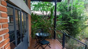 A balcony with a table and chairs, surrounded by lush greenery and a brick wall.