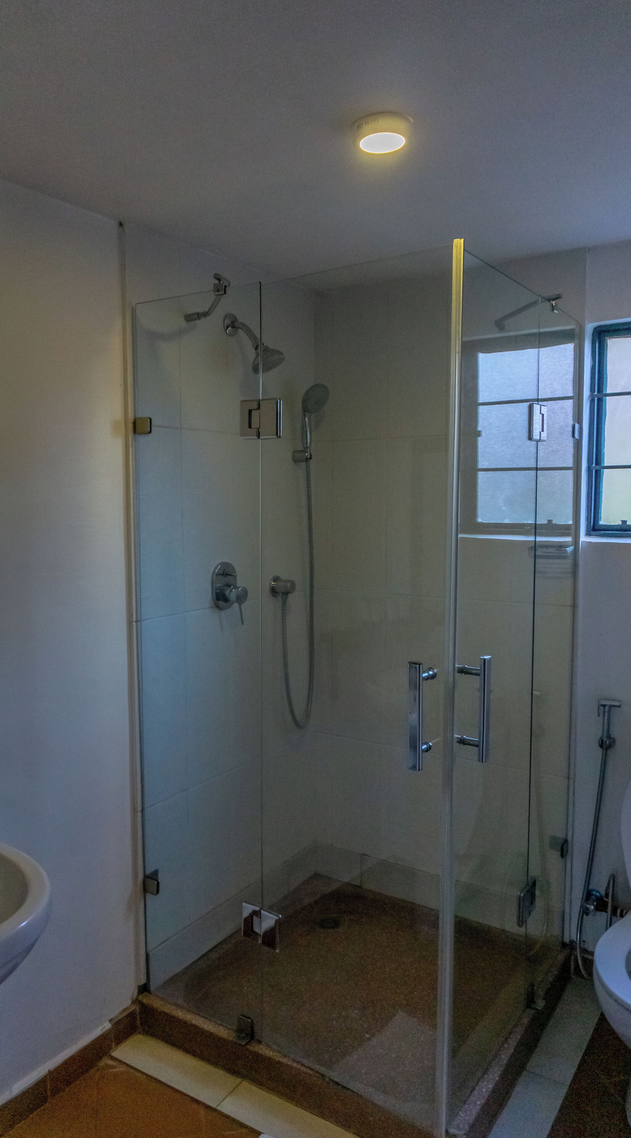 A glass-enclosed shower with a handheld showerhead and a wall-mounted faucet.