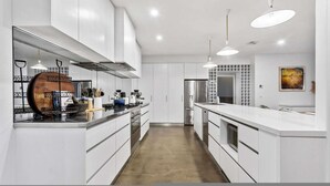 Une cuisine moderne avec des meubles blancs, des appareils en acier inoxydable et des luminaires suspendus.