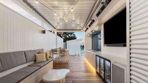 Un intérieur moderne avec une terrasse en bois, un canapé, une table à manger et un téléviseur fixé au mur.