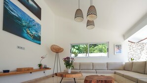 Un salon moderne avec un grand tableau, une table basse en bois, une table ronde, un canapé et des lampes suspendues.