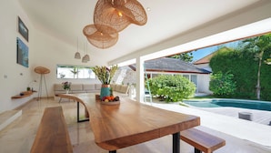 Un vaste espace de vie doté d’une longue table en bois, de bancs et de luminaires suspendus en osier.