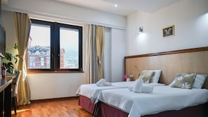 Une chambre d’hôtel avec deux lits, un plancher en bois, une fenêtre avec des rideaux et une vue sur des immeubles.