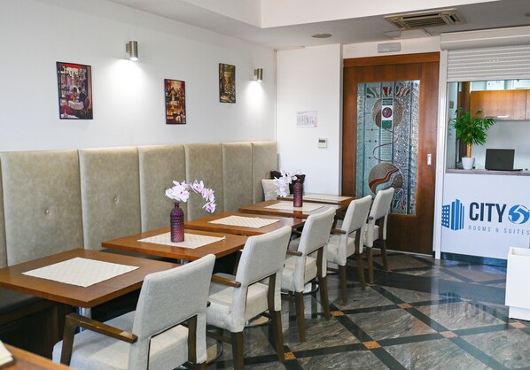 A hotel lobby with a seating area, tables, chairs, and a reception desk.