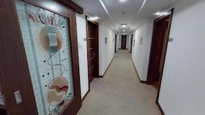 Un couloir d’hôtel avec un sol recouvert de moquette, des portes en bois et un motif décoratif sur le mur.