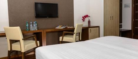 A hotel room with a bed, two chairs, a desk with a flat-screen TV, and a wardrobe.