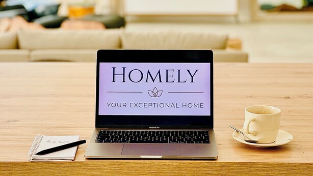 Una laptop sobre una mesa de madera mostrando el texto "HOMELY YOUR EXCEPTIONAL HOME".