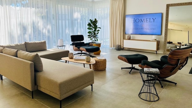Een moderne woonkamer met een beige bank, een zwarte stoel, een houten salontafel en een televisie met daarop de tekst 
