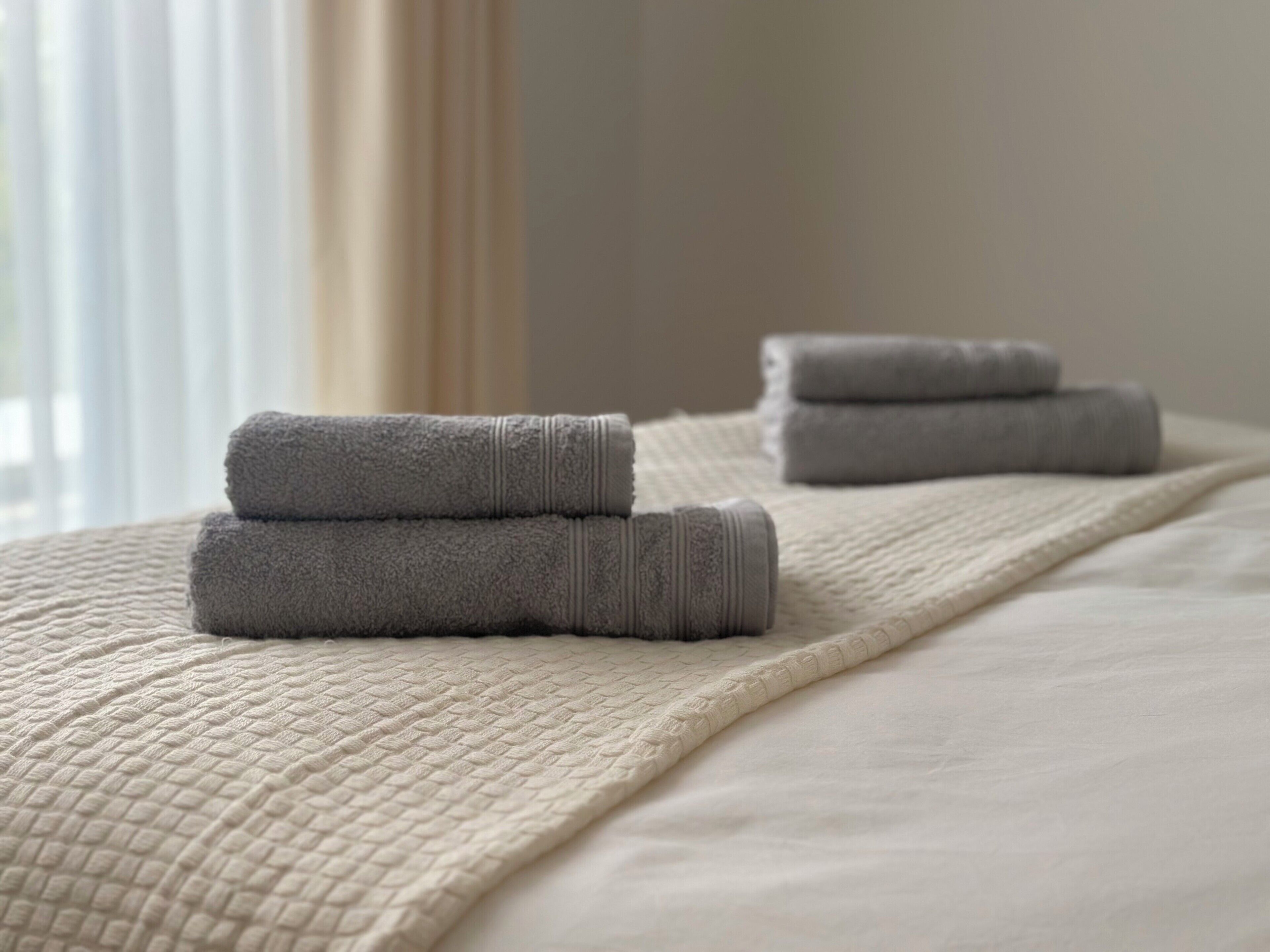 A neatly made bed with a textured beige blanket and two folded gray towels.
