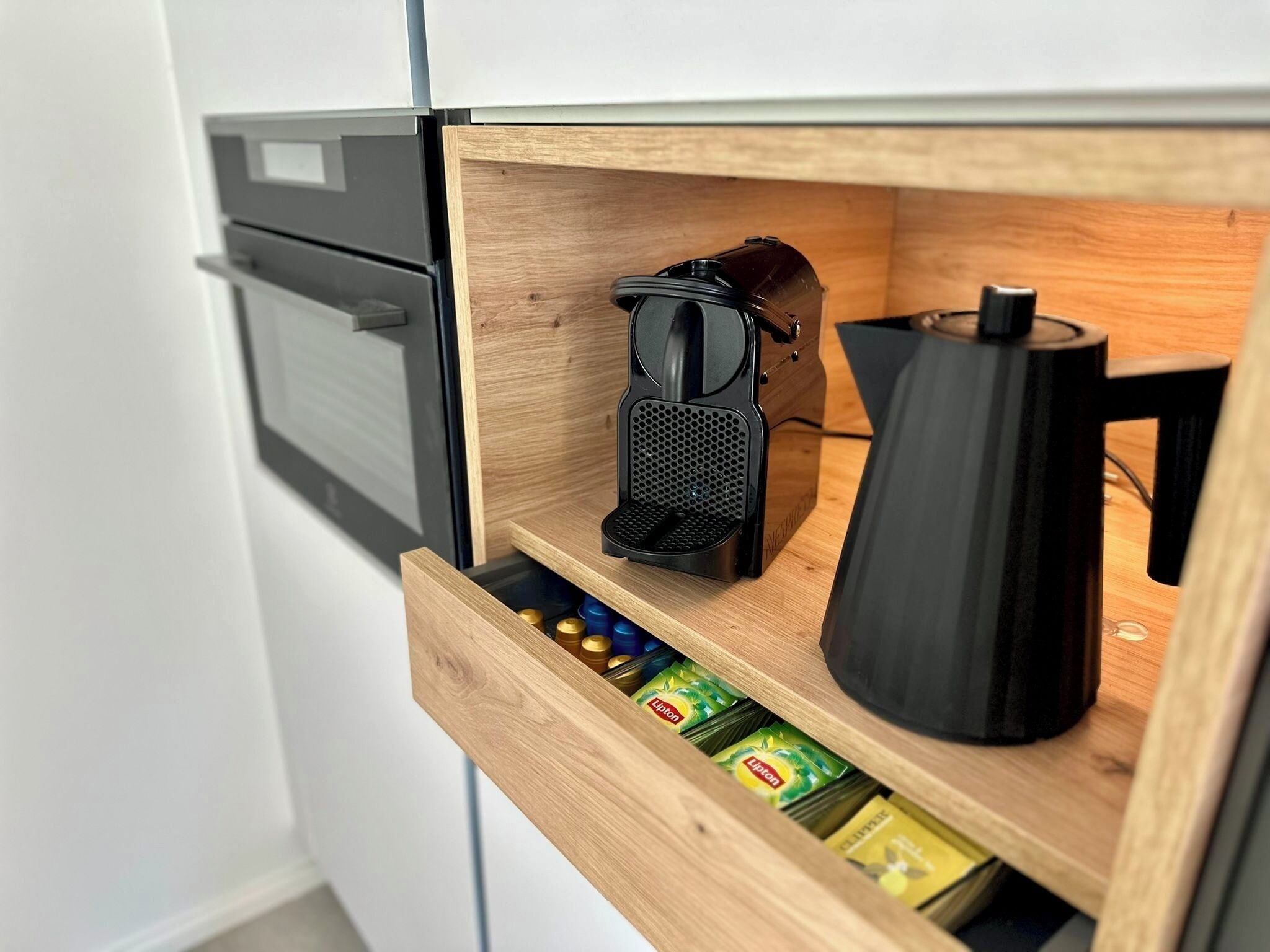 Eine Hollauszug mit einer schwarzen Kaffeemaschine, einem schwarzen Wasserkocher und einer Packung Lipton Tee.