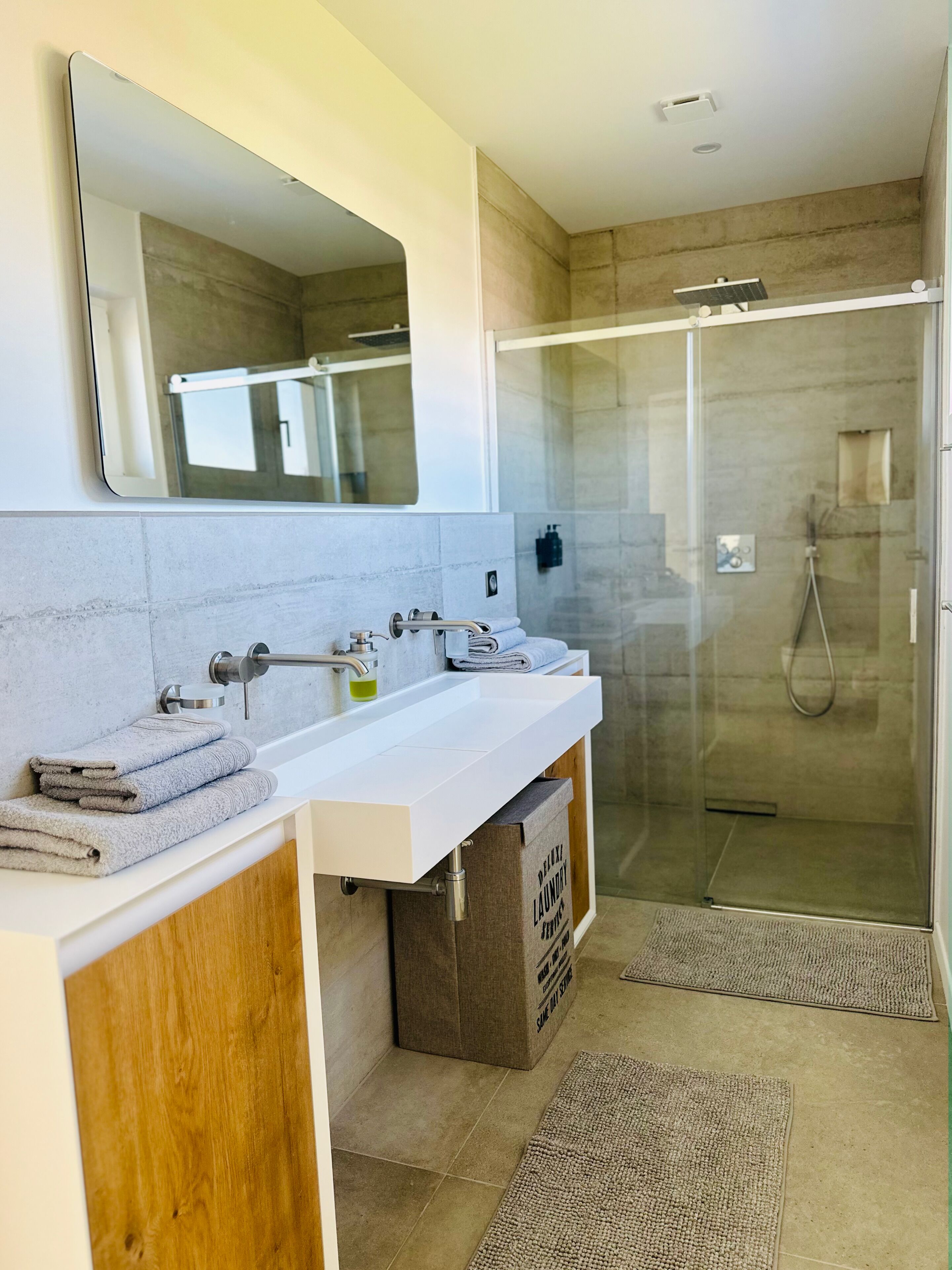 Ein modernes Badezimmer mit Duschkabine aus Glas, einem weißen Waschbecken und einem Holz-Waschtisch.